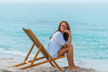 A fair girl in pink glasses is resting on a sun lounger, on the sea