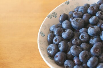 Close-up of fresh organic antioxidant blueberries in a white and bleu porcelain bowl on a wooden table.