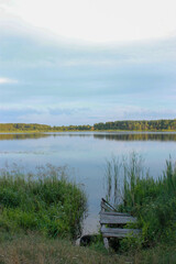 the village in summer. View of a clear uninhabited lake with an old bridge