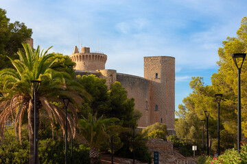 Fototapeta na wymiar Exterior de castillo de Bellver, en Palma de Mallorca, visto de cerca, con palmeras, pinos y farolas junto al camino de entrada. Mallorca, Islas Baleares, España.