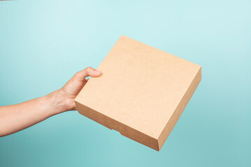 Mockup. Female hand holding brown rectangular cardboard box on light blue background. Woman give...
