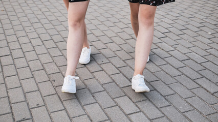 Two girlfriends in white sneakers walk down the street.