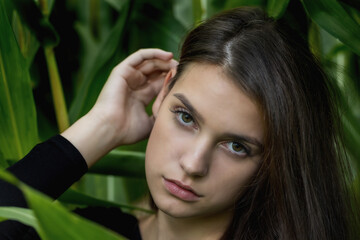Closeup portrait of brunette young woman posing among the green plants