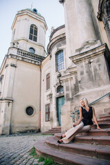 A young, blonde girl in a black blouse and sunglasses poses against the backdrop of an old courtyard in Lviv. Ukraine.