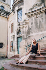 Fototapeta na wymiar A young, blonde girl in a black blouse and sunglasses poses against the backdrop of an old courtyard in Lviv. Ukraine.