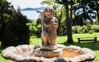 Ancient fountain with a statue of a stone angel praying in the beautiful garden of Folly Arboretum by Lake Balaton in Badacsony, Hungary, Europe.