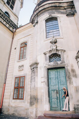 Fototapeta premium A young, blonde girl in a black blouse and sunglasses poses against the backdrop of an old courtyard in Lviv. Ukraine.