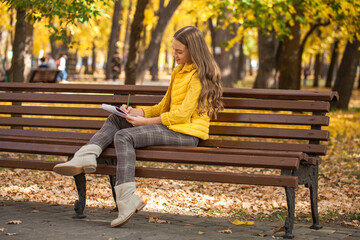 Young beautiful girl with a sketchbook sits on a bench in the autumn park
