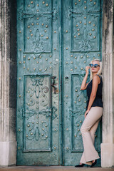 A young, blonde girl in a black blouse and sunglasses poses against the backdrop of an old courtyard in Lviv. Ukraine.