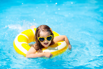 Child in swimming pool on ring toy. Kids swim.