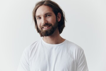 Portrait of a cheerful man with a black thick beard and long hair with a kind smile in a white T-shirt on a white isolated background