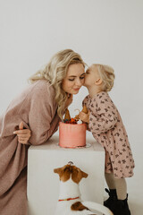 Mom with a little daughter in the studio eat a cake, hug and kiss. Girl's birthday.