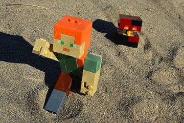 Obraz premium LEGO Minecraft large action figure of Alex chased by hostile mob Magma Cube on sandy desert landscape in afternoon sunshine. 
