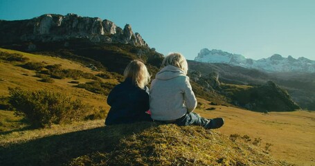 Brother and sister sitting on the hill on springtime vacation travel. Children together enjoying epic nature landscape on journey at evening. Child boy and girl with blonde hair on weekend