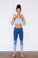 Fototapeta na wymiar Home Sport. Portrait African american woman exercising with dumbbells and enjoying fitness and healthy lifestyle