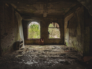 Arched windows in a dark decaying abandoned old room. Crumbling wall inside a dark abandoned room. Walk through the old ruins. Ghost town. War torn place