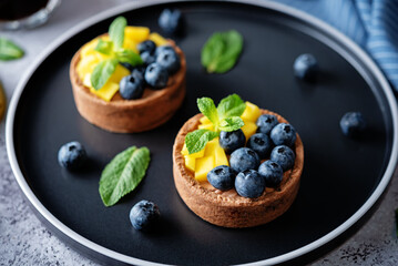 Chocolate tartlets with chocolate cream filling and mango fruit with blueberries - obrazy, fototapety, plakaty