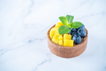 Chocolate tartlets with chocolate cream filling and mango fruit with blueberries