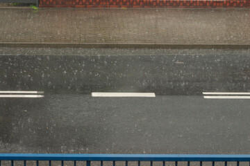 Asfaltowa droga w czasie deszczu. Czarna nawierzchnia pokryta jest warstwą wody rozbijanej przez krople intensywnie padającego deszczu. Pośrodku jezdni jest biała linia. © boguslavus