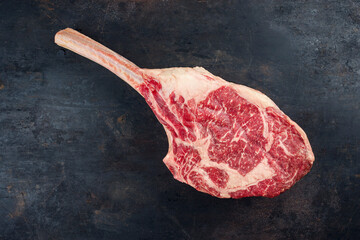 Raw dry aged wagyu tomahawk steak offered as top view on an old black rustic board with copy space