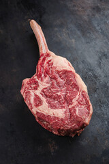Raw dry aged wagyu tomahawk steak offered as close-up on an old black rustic board with copy space