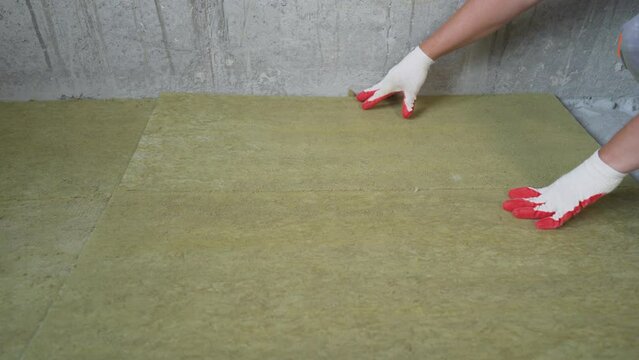 Laying glass wool on a concrete floor. The builder insulates the floors of the house with glass wool.