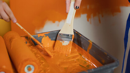 Mom and kid painting walls with orange color and paintbrush, using renovating diy tools at home. People working on redecoration improvement with paint and equipment. Close up.
