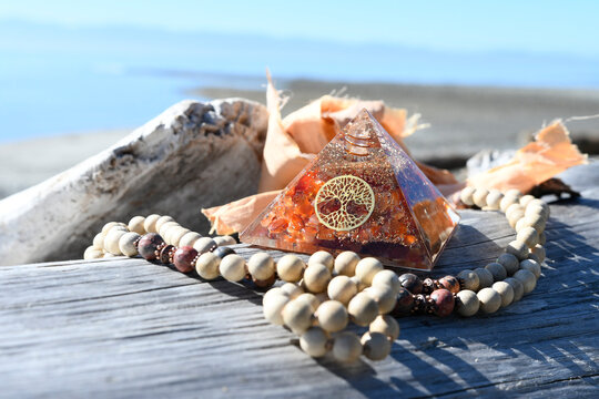 A close up image of a orgonite pyramids made with red carnelian crystals along with a wooden mala necklace. 