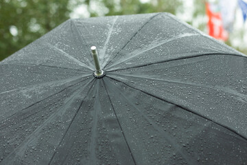 Black umbrella in rain. Large umbrella in bad weather. Raindrops on black material.