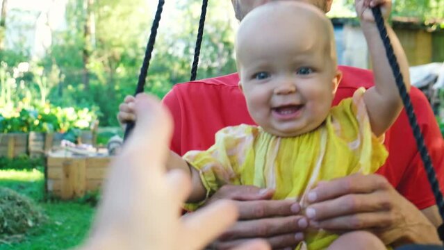 POV happy smiling little toddler daughter is swinging on swing with her father in backyard. Dad and daugher spending time together.