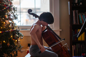 An expressive child plays cello by Christmas tree at home