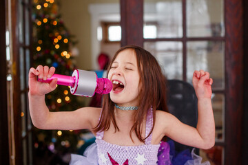 A girl in costume sings into a microphone by Christmas tree