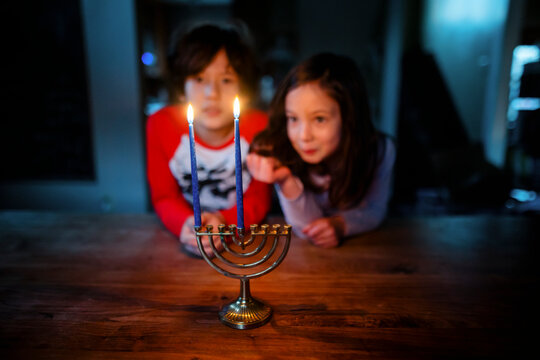 Two siblings sit at table together staring at lit candles on menorah