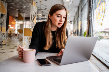 young girl in a cafe by the window working on a laptop