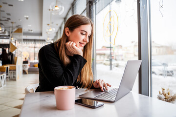 girl in a cafe with a cup of coffee on a laptop - obrazy, fototapety, plakaty