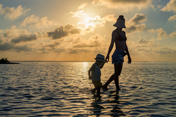 Silhouette of a woman and her baby boy walking in the water at sunset