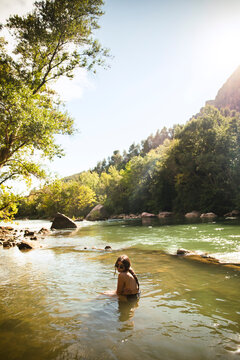 Naked girl bathing in a river surrounded by trees during sunset