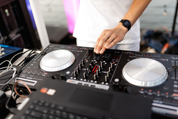 DJ plays live set and mixing music on turntable console at stage in the night club. Disc Jokey Hands on a sound mixer station at club party. DJ mixer controller panel for playing music and partying.
