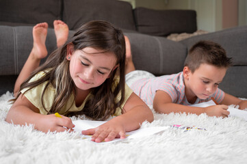Obraz na płótnie Canvas Siblings playing together at home. little boy and girl lying on the carpet and drawing on white sheets of paper with colorful crayons. High quality photography.