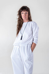 Portrait of a woman dressed in white yoga clothes over white background wearing a japa mala while looking at camera.