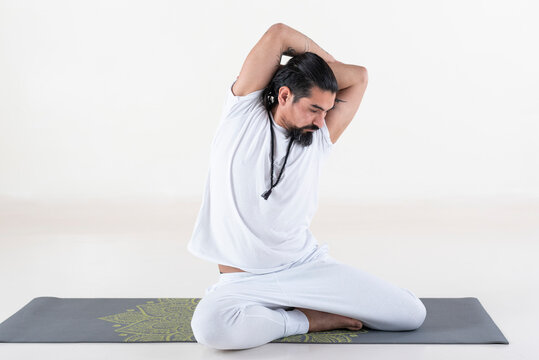 A man dressed in white doing yoga on a mat over white background. .bharadvajasana yoga pose.