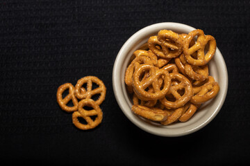 Pretzels inside a small bowl next to three pretzels on a black background