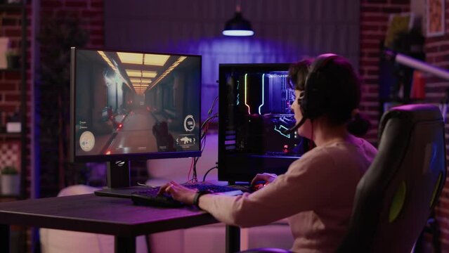Gamer girl using pc setup playing multiplayer first person shooter talking on headset while explaining gameplay to subscribers. Woman streaming online action game while sitting in gaming chair.