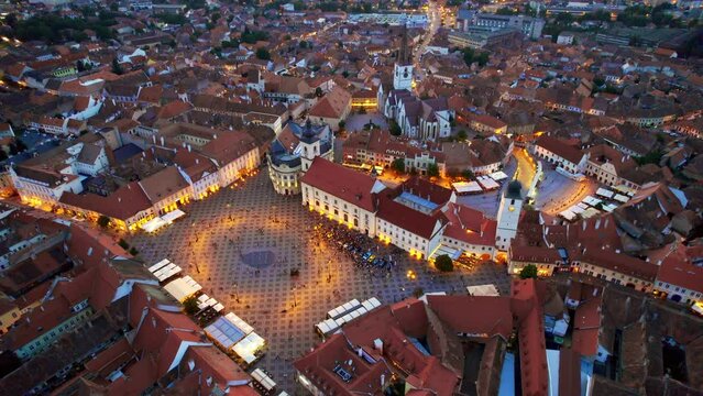 Aerial drone view of the Historic Centre of Sibiu at sunset, Romania. The Great Square with Sibiu Lutheran Cathedral and old buildings around, narrow streets, illumination