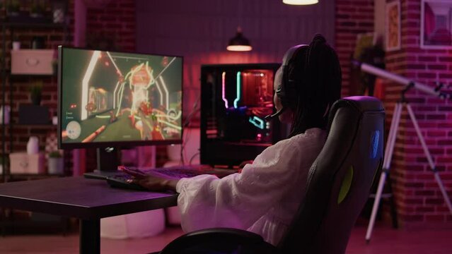 Over shoulder view of woman streaming first person shooter doing victory hand gesture after win in tournament. African american gamer girl surprised after winning online competition on gaming pc.