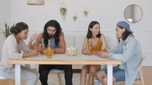 a group of friends are sitting on a table, drinking beer, when a guy comes and checks with bottles, why beer foams and pours out of the bottle