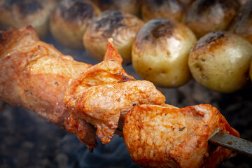 Outdoor street food. Marinated pork shashlik and potatoes roasted on a charcoal grill. A traditional Caucasian dish. Close-up