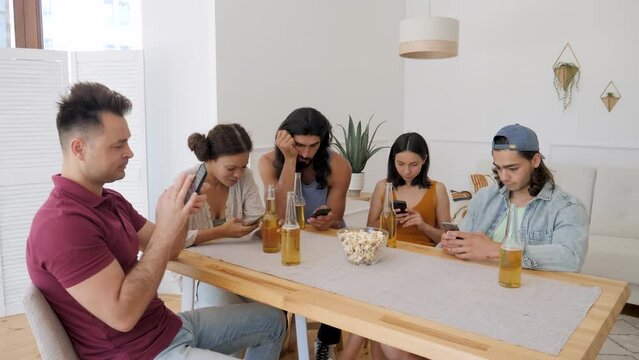 a group of friends are sitting on their phones sitting at the table at home