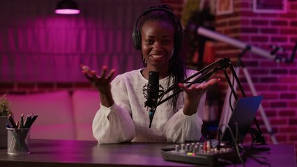 African american woman vlogger talking to audience while recording podcast using audio mixer and microphone. Famous influencer creating content for online social media page from podcasting studio. - Powered by Adobe