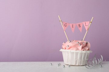 Baby shower cupcake with pink cream and Girl topper on white table against violet background, space...